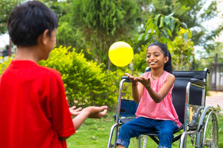 Happy young brother playing with his sister while using wheelchair at park - concept of happines, inspirational and family supportの写真素材