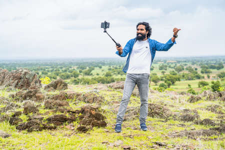 full shot of travel vlogger on top of mountain recording video on mobile phone of soical media -...