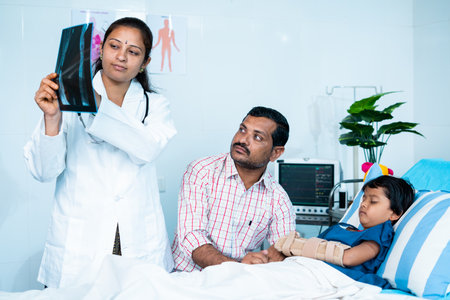 Doctor explaining kids x ray report about broken hand to father at hospital before surgery - concept of pediatrician, childcare service and injury.の写真素材