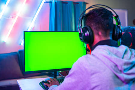 shoulder shot of professional gamer playing live video game on green screen monitor by talkng on headphones - concept of entertainment, excitement and cyberspace.の写真素材