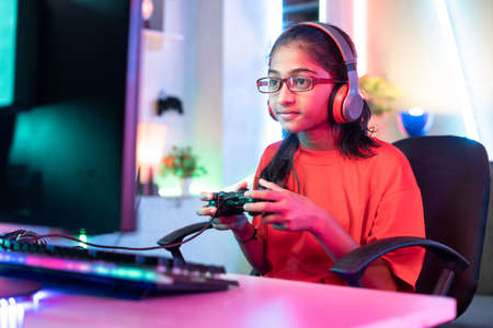 girl kid with wireless headset playing online video game on computer using joystick at home - concept of entertainment, gaming addiction and tournamentの写真素材