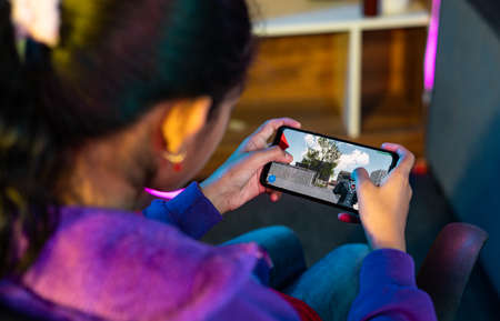 Shoulder shot of girl playing live video game on mobile phone at home - concept of relaxation, championship and tournament.の写真素材