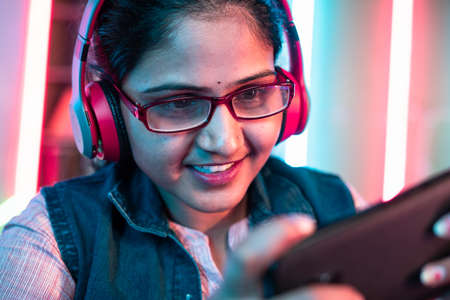 Close up shot of girl with headphones and eyeglass playing online video game on mobile phone at home - concept of live streamer, holydays and cyberspaceの写真素材