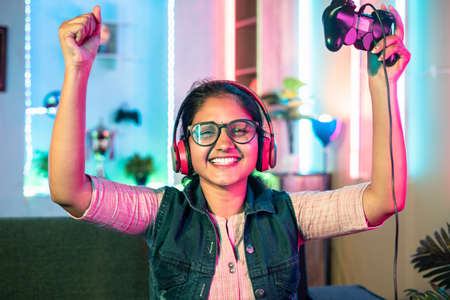 Excited woman celebrating for win while playig video game on sofa using game pad by looking camera at home - concept of leisure activities, entertainment and happiness.の写真素材