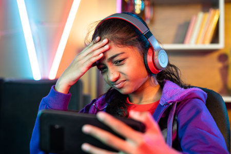 Sad girl with headphones losing game while playing video game on mobile phone at home - concept of competition, technology and entertainmentの写真素材