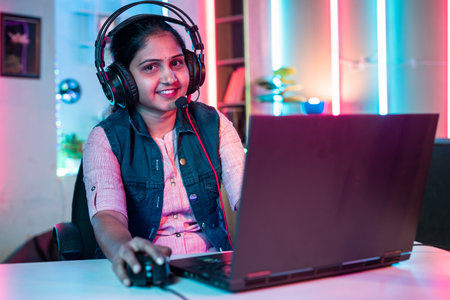 Smiling girl gamer looking at camera while playing live video game on laptop at home on neon background - concept of vlogger, cyber space and championshipの写真素材