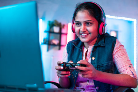 Confident girl with headset playing video game on laptop using joystick at home - concept of leisure...