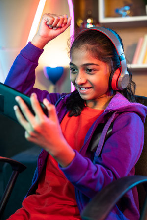 vertical shot of Excited teenager girl with headset celebrating win while playing video game on mobile phone at home - concept of achievement, competition and tournament.の写真素材