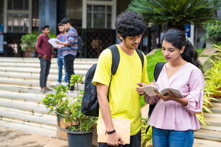 Serious indian teenager students preparing for exams by reading books at college campus - concept of knowledge, education and competitionの写真素材