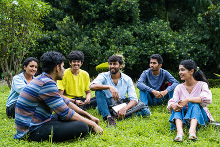 Group of happy students having chat with each other while sitting on college campus park - concept of takng break, communication and development.の写真素材