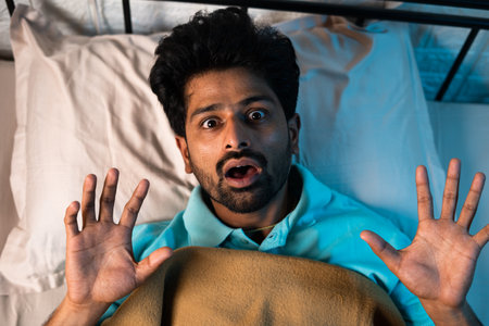 young man suddenly wakes up during night while sleeping on bed - concept of nightmares, bad dreams and illness or diseaseの写真素材