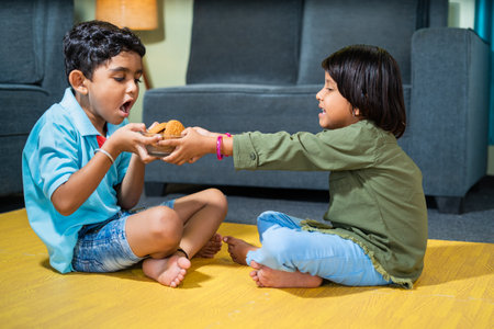 Young siblings kids fighting for snacks or biscuit while sitting on floor at home - concept of childhood lifestyle, relationships and weekend holidaysの写真素材