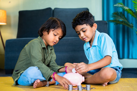 Happy teenager siblings putting coin on piggy bank while sitting on floor at home - concept of...