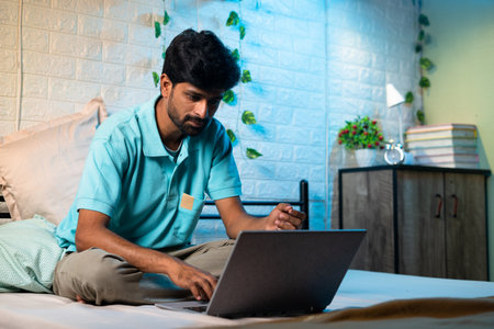 young man busy woking on laptop uring night on bed - concept of over working, work from home and project deadlineの写真素材