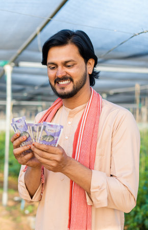 vertical shot of Happy smiling young farmer at greenhouse couting money or currency notes - concept of successful business, agronomy and financial or bankingの写真素材