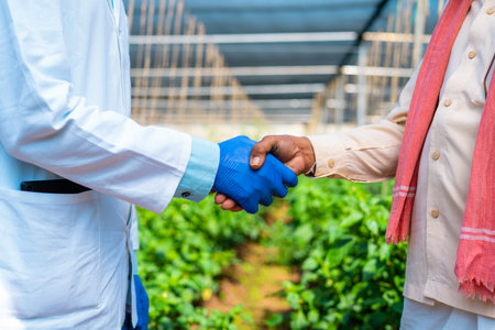 Close up shto of agro scientist greeting by shaking hands to Indian farmer at greenhouse - concpet...