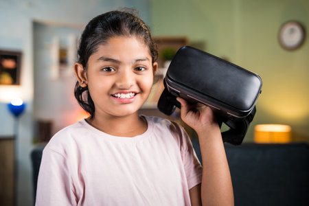 portriat shot of Happy smiling girl kid with Vr or virtual reality headset in hand looking camera at...