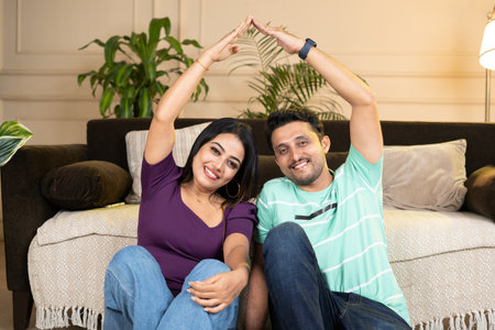 happy smiling couple showing by making home roof gesture by joining hands while looking at camera at there new home or apartment - concept of new home, future planning and insurance protection.の写真素材