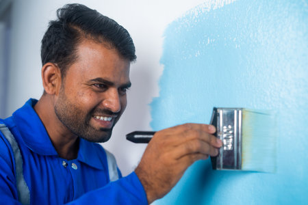 Close up shot of smiling painter painting on wall with paint brush on white wall - concept of professional occupation, blue collar jobs and employmentの写真素材