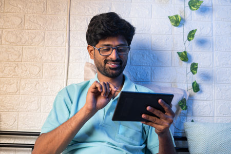 happy young man on bedroom using digital tablet at home before sleeping - concept of social media addiction, internet and cyberspaceの写真素材