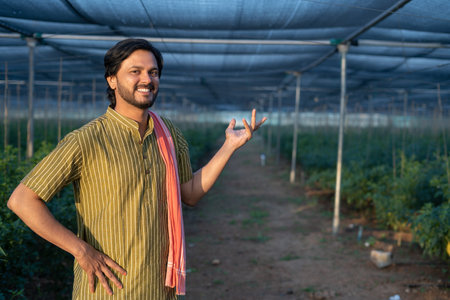 Portrait shot of happy smiling famer showing greenhouse by loooking at camera - concept of...