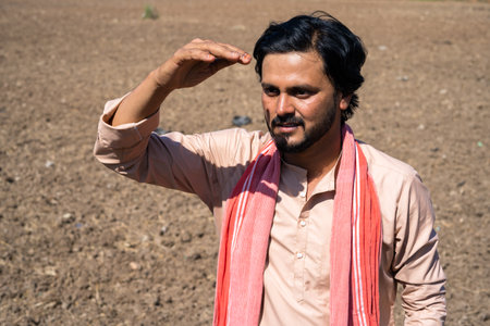 Sad Indian farmer stadning at Barren agricultural farmland at hot sunny day looking far away for...