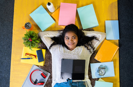 Top view flatlay shot of thoughtful girl sleeping with books around on floor by looking at camera while reading at homeの写真素材