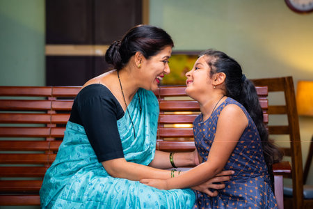 Happy mother playing with daughter by cuddling while sitting on sofa at home - concept of motherhood, family bonding and weekend holidays.の写真素材