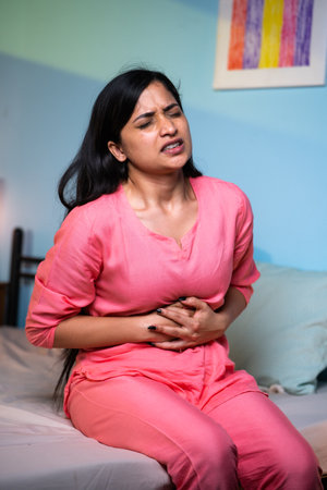 Vertical shot of girl suffering from stomach pain during late night at home - concept of menstruation cycle, health problems and unwellの写真素材