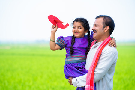 Happy village girl kid playing with airplane toy while father holding or carrying near farmland - concept of relationship, parental caring and healthy lifestyleの写真素材
