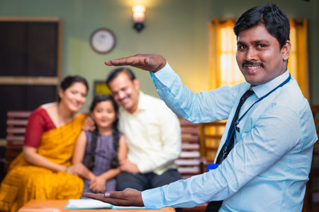 Happy indian banker showing hands like holding family using hand gesture by looking camera at home - concept of insurance protection, banking service and banking securityの写真素材