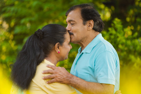 Happy senior man or husband kissing his wifes forehead by hugging at park - concept of emotional bonding, physical intimacy and romantic moment.の写真素材