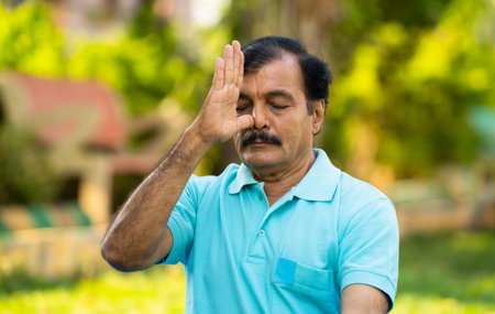 Elderly Indian senior man doing nostril breathing yoga or pranayama exercise - concept of zen, healthy lifestyle and mental wellnessの写真素材