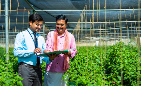 Happy indian bank officer taking sign from farmer to loan approval banking documents at greenhouse -...
