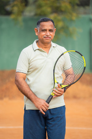 vertical shot of Happy smiling senior men with racquet and ball looking camera at tennis court - concept of confident, successful and relaxationの写真素材