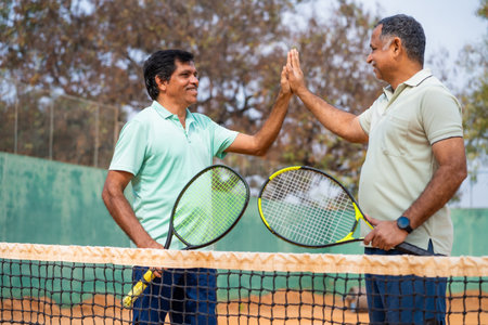 Indian two senior players celebrating by giving Hi-fi after winning tennis game at court - concept...