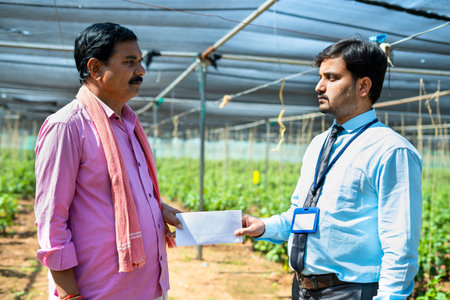 Indian bank officer giving notice to farmer at greenhouse - concept of debt, financial problems and loss in business.の写真素材