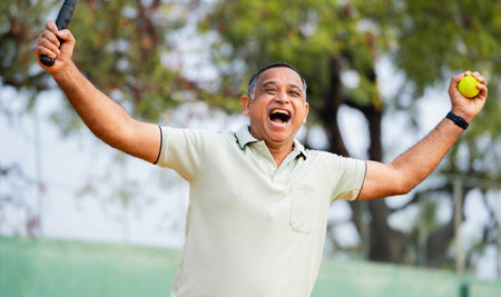 Indian excited senior man celebrating by shouting after winning tennis match at court - concept of competition, energetic and fitness lifestyle.の写真素材