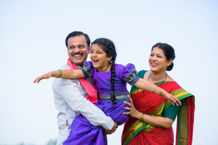 Playful excited indian girl kid while holding by father with mother near farmland - concept of parents support, family bonding and happinessの写真素材