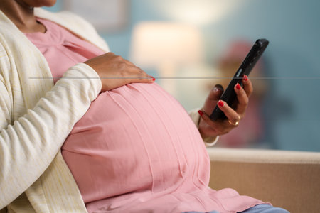 Close up shot of indian pregnant woman busy using mobile phonw by holding tummy at home - concept of digital connection, technology and Digital maternityの写真素材