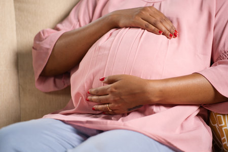 Close up shot of indian pregnant woman feeling by touching tummy while sitting on sofa at home - concept of motherhood, expecting and prenatal bondingの写真素材
