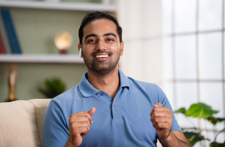Happy indian man talking by looking camera on video call while sitting on sofa at home - concept of Virtual connection, Online interaction and Digital communicationの写真素材