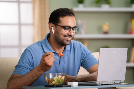 Happy indian man eating fruits salad while talking on online video call at home - concept of healthy eating, Video conference and Remote conversationの写真素材