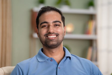 Happy smiling indian man looking at camera while sitting on sofa at home - concept of successful, relaxation and satisfactionの写真素材