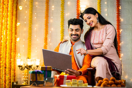 Happy young indian couple busy checking laptop during festival celebration at home - concept of sales or offers, buying new apartment and planningの写真素材