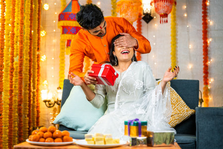 Happy brother by closing eyes giving surprise gift to sister during raksha bandhan festival celebration at home - concept of relationship bonding, togetherness and family ceremony.の写真素材