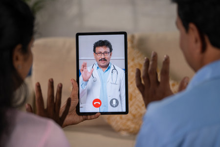 Shoulder shot of middle aged Indian couple consulting doctor on video call using digital tablet at home - concept of Telemedicine, Virtual medical diagnosis and Online Health Check up.の写真素材