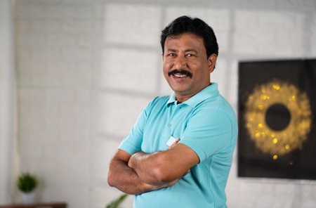 Confident Happy middle aged indian man standing with arms crossed by looking at camera home -...