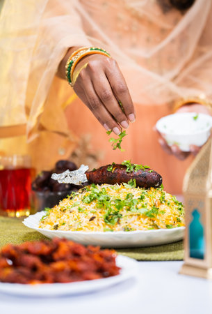 Vertical shot close up shot of indian woman hands adding toppings or coriander on top of biryani during iftar dinner at home - concept of iftar dinner, preparation and yummy food.の写真素材
