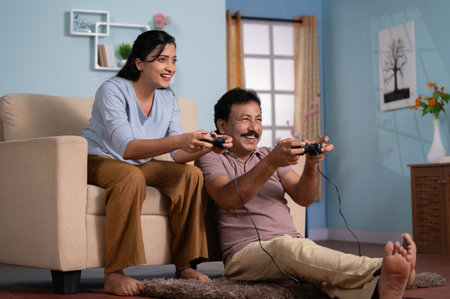 Cheerful indian father with adult daughter playing video game by using joystick at home - concept of...